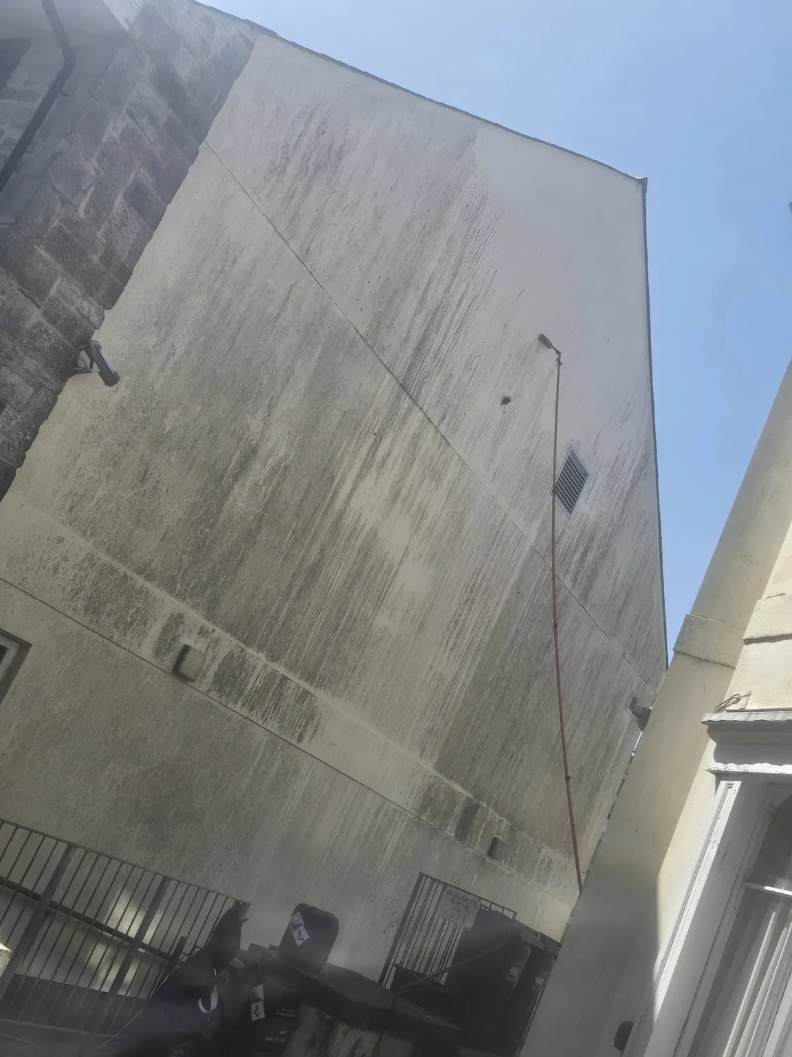 Tall rendered gable end before cleaning, streaked grey and green with run-off marks and organic growth